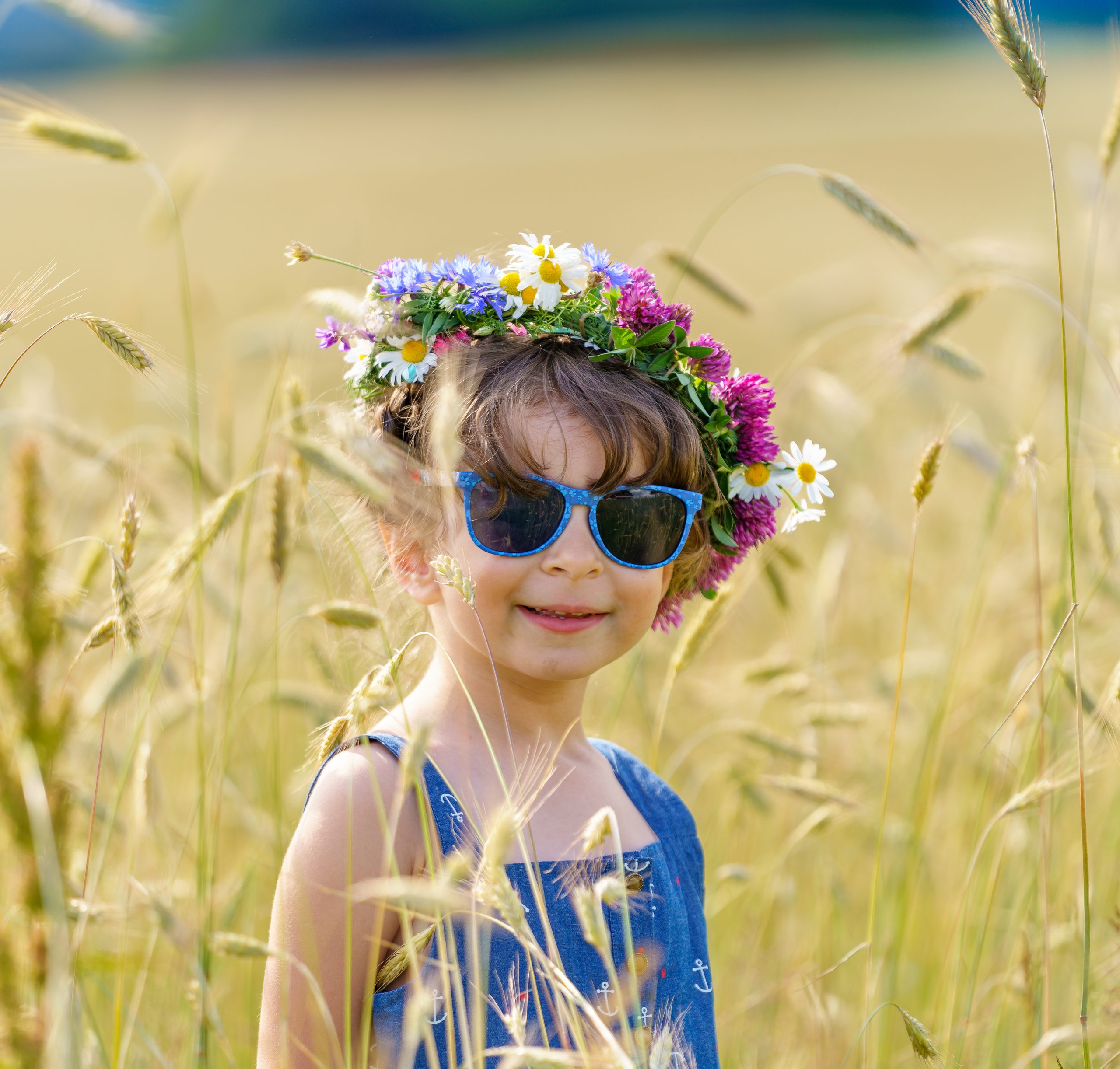 Niña con corona de flores y gafas de sol azules en un trigal