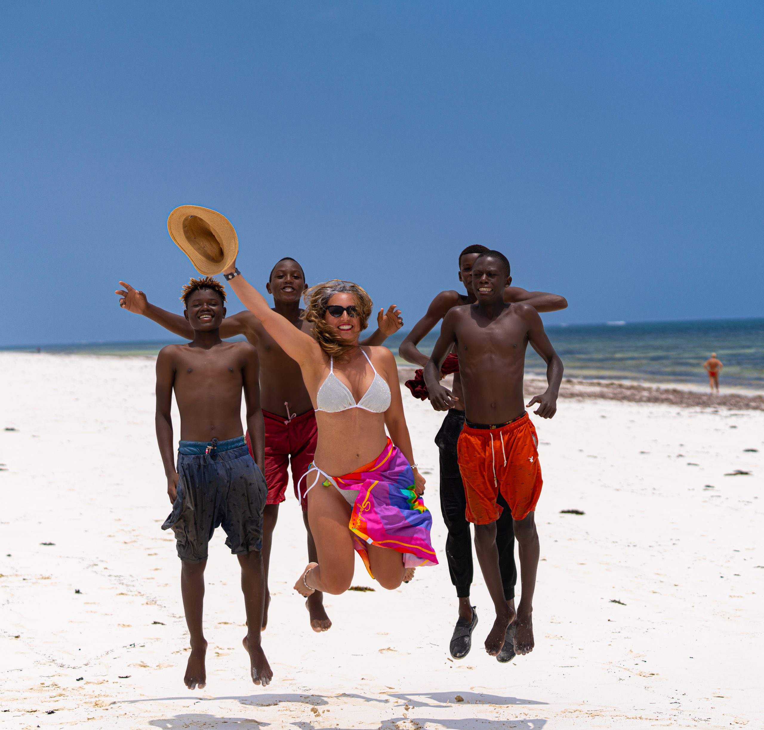 Femme en bikini sautant sur une plage blanche avec trois jeunes hommes