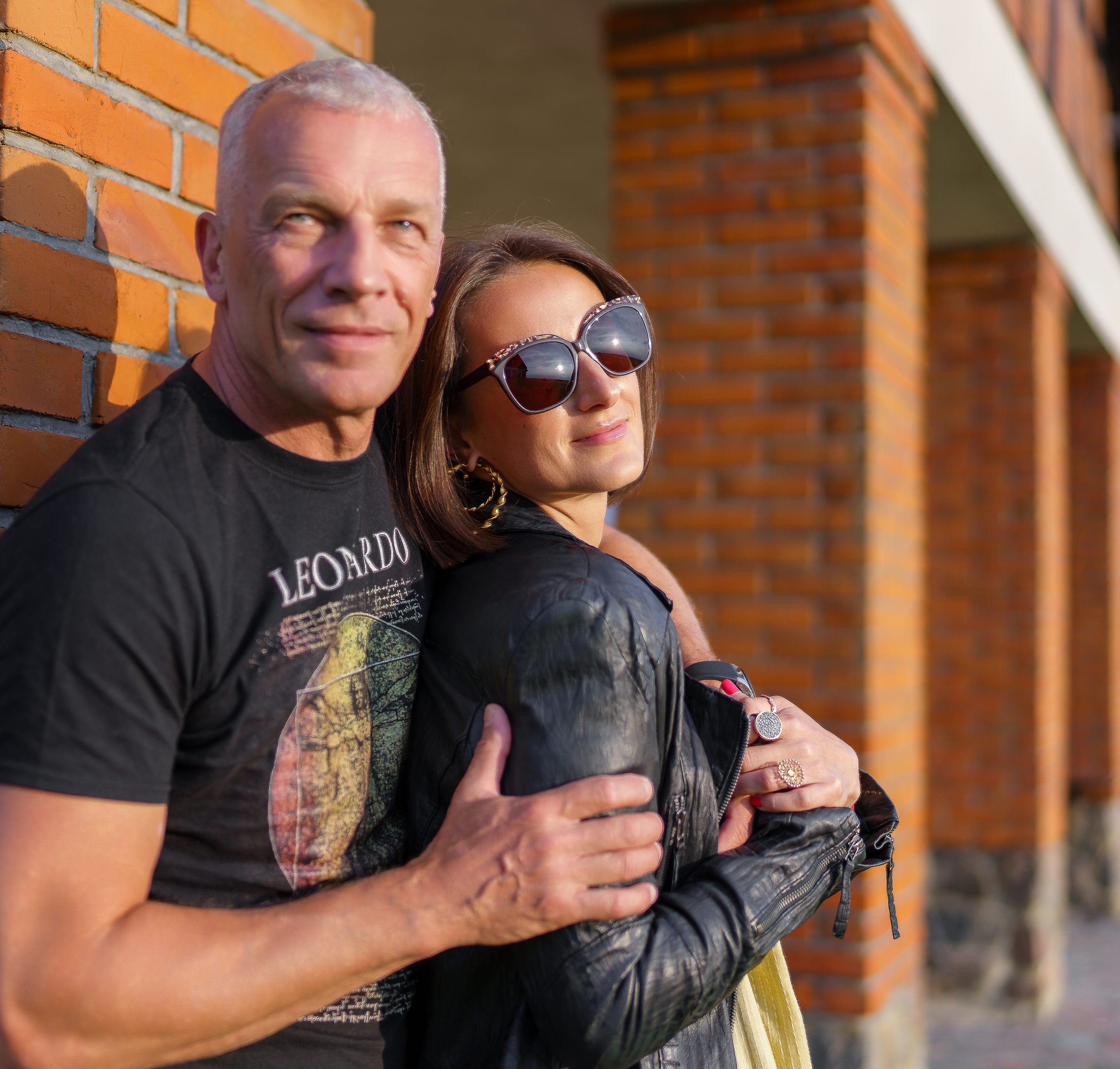 Couple enlacé devant des arcades en briques, elle en lunettes de soleil