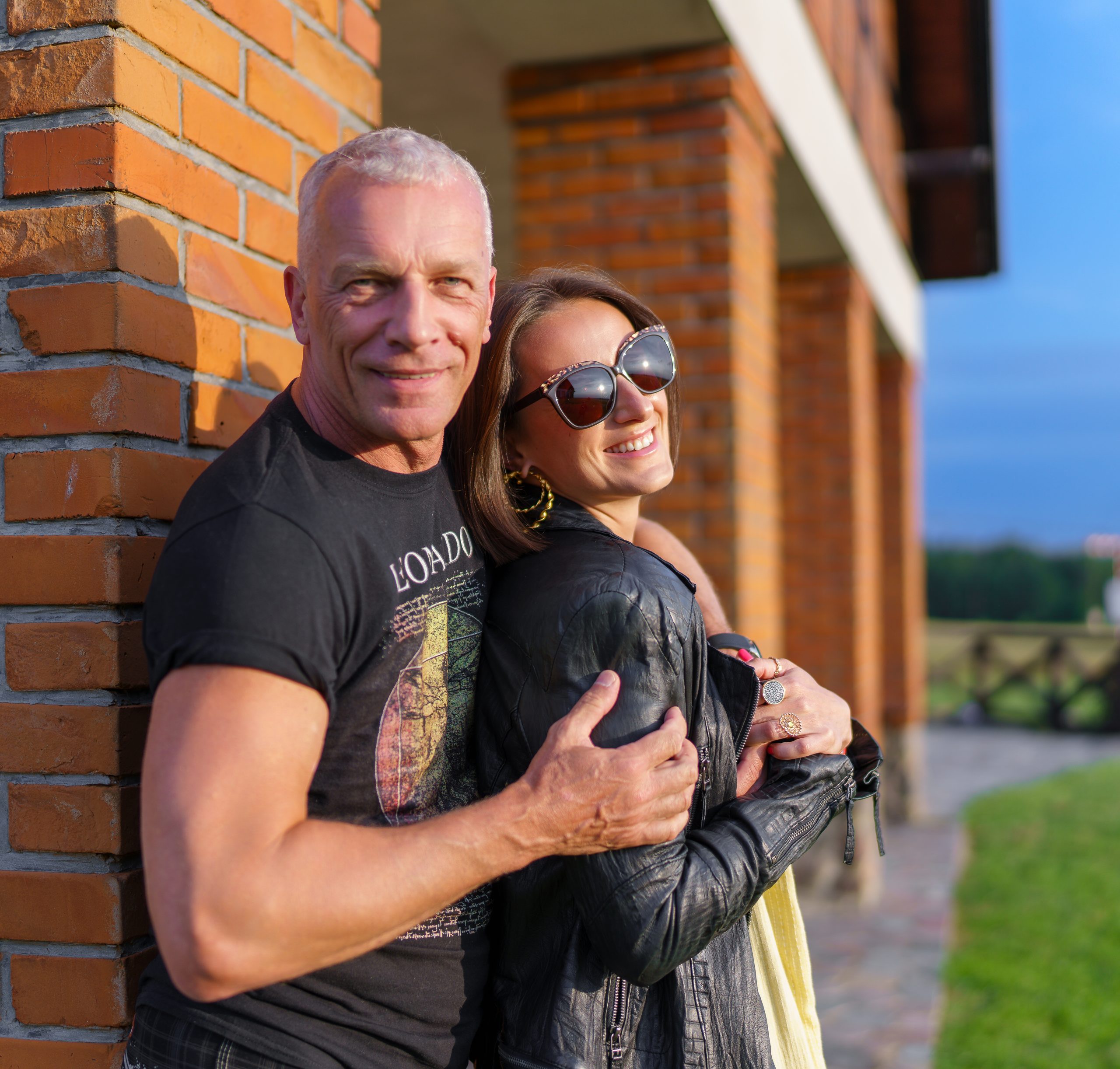 Couple enlacé contre un mur de briques, la lumière du soir sur leurs visages