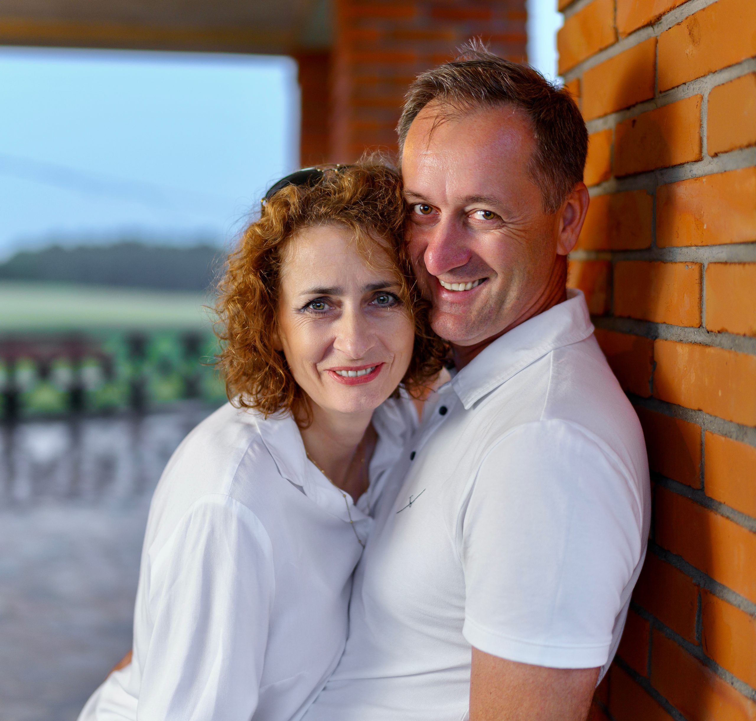Portrait rapproché d'un couple souriant en blanc près d'un mur de briques