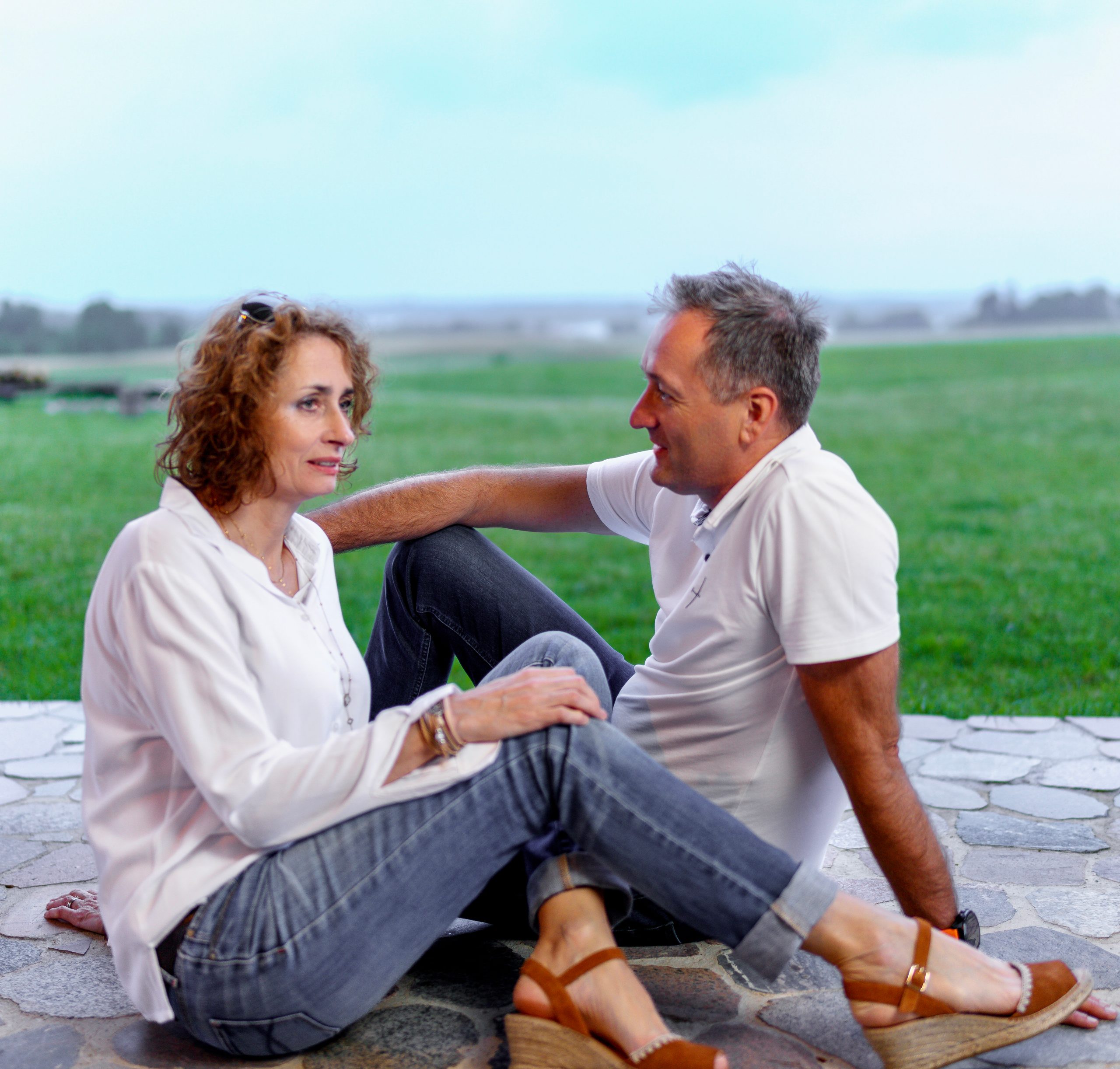 Couple en blanc et jean assis sur l'herbe, en train de discuter