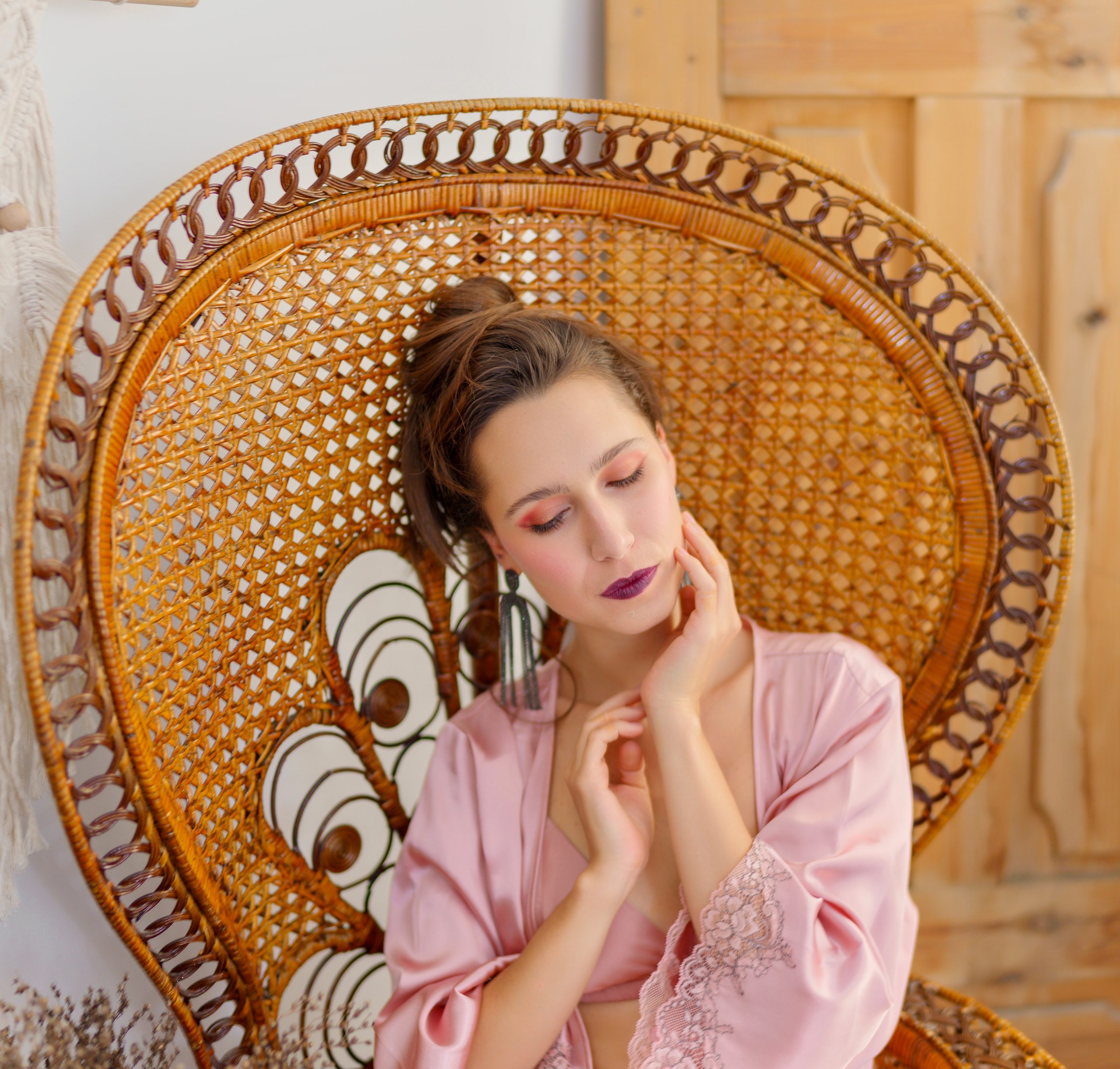 Femme en peignoir de satin rose assise dans un fauteuil paon en osier