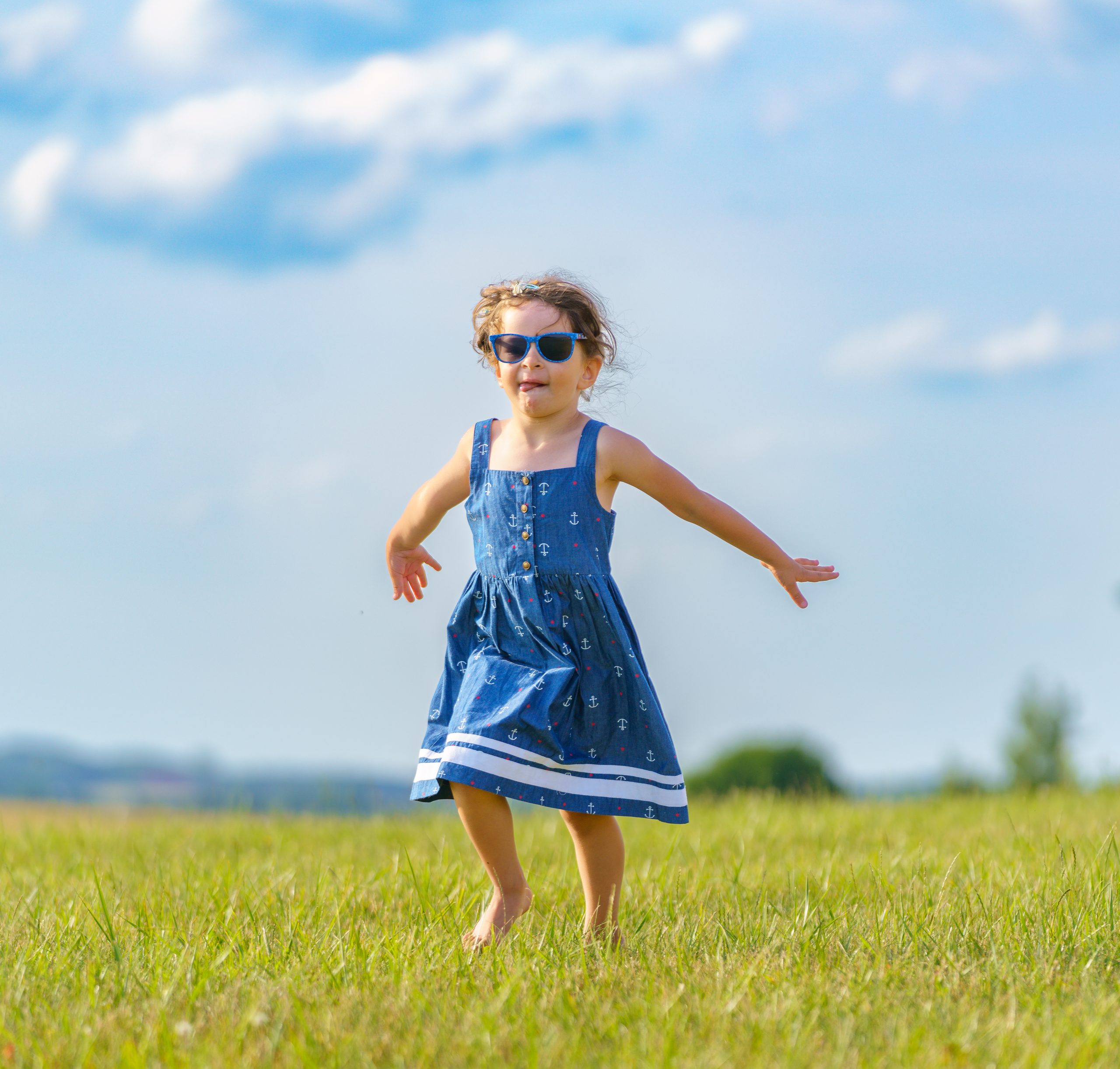 Niña corriendo descalza por un prado con los brazos abiertos