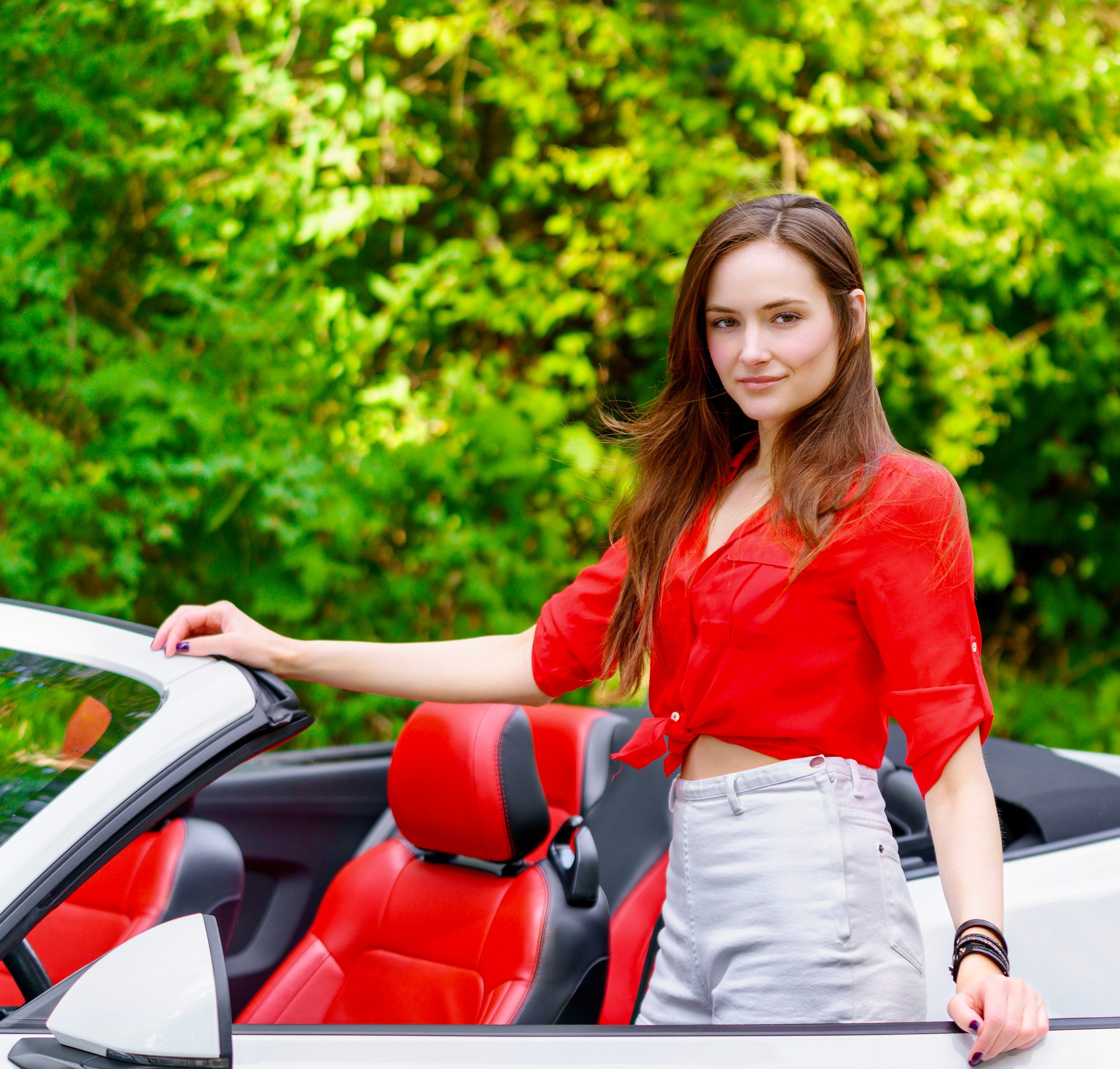 Mujer con camisa roja junto a un descapotable blanco de asientos rojos