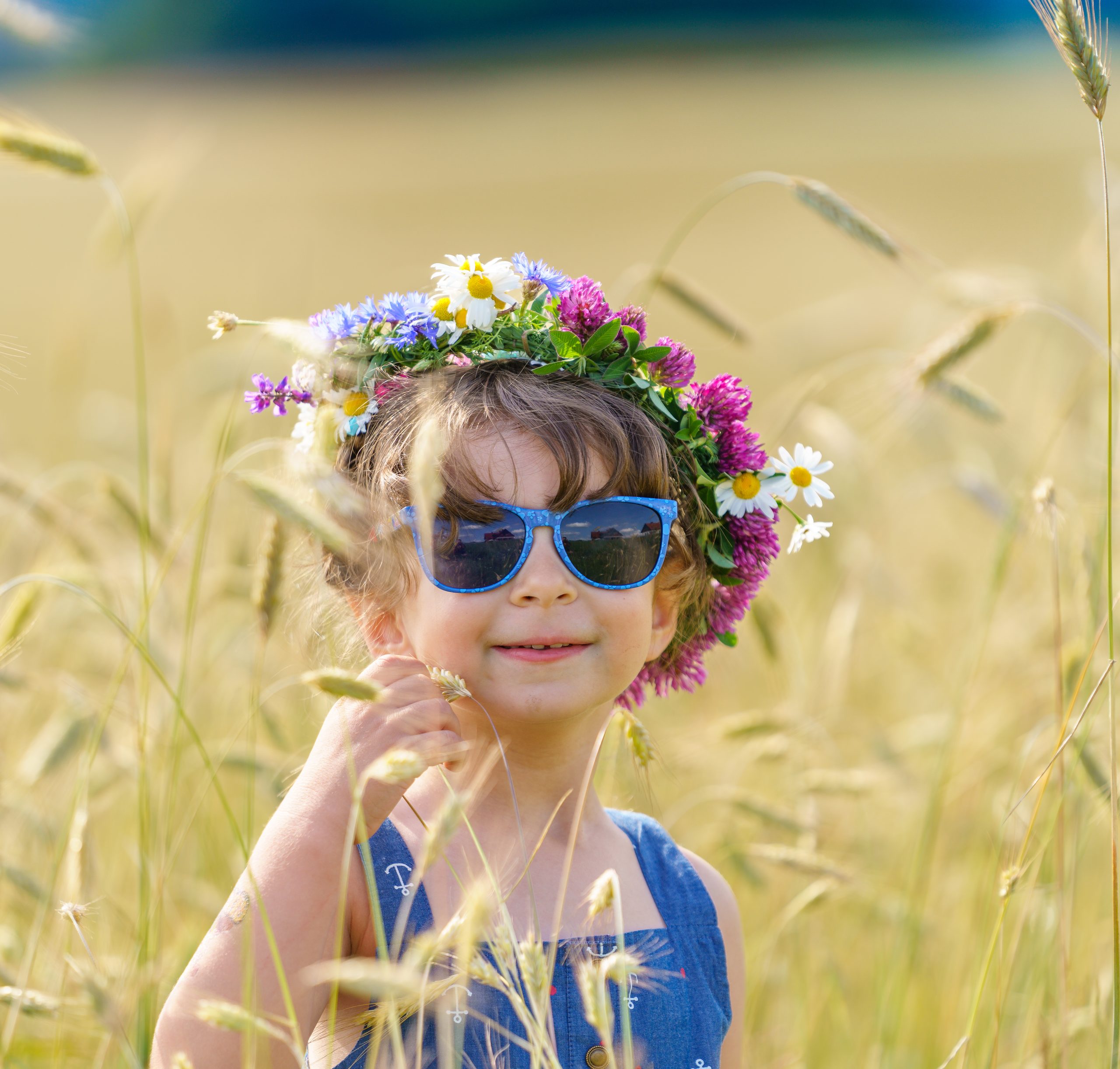 Niña sonriente con corona de flores entre el trigo alto