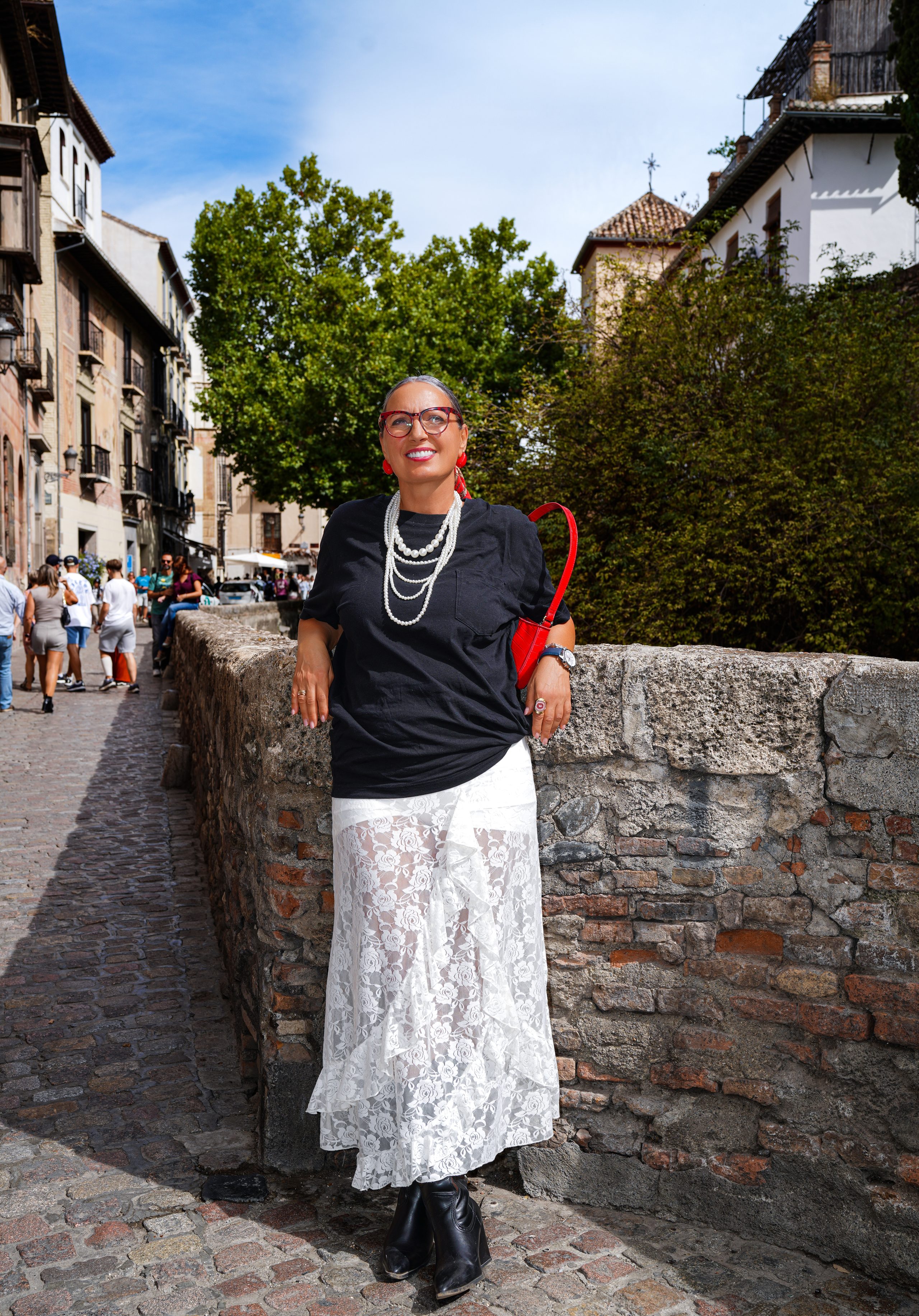 Kobieta oparta o kamienny murek przy uliczce wzdłuż rzeki, w tle stare domy — Carrera del Darro, Granada