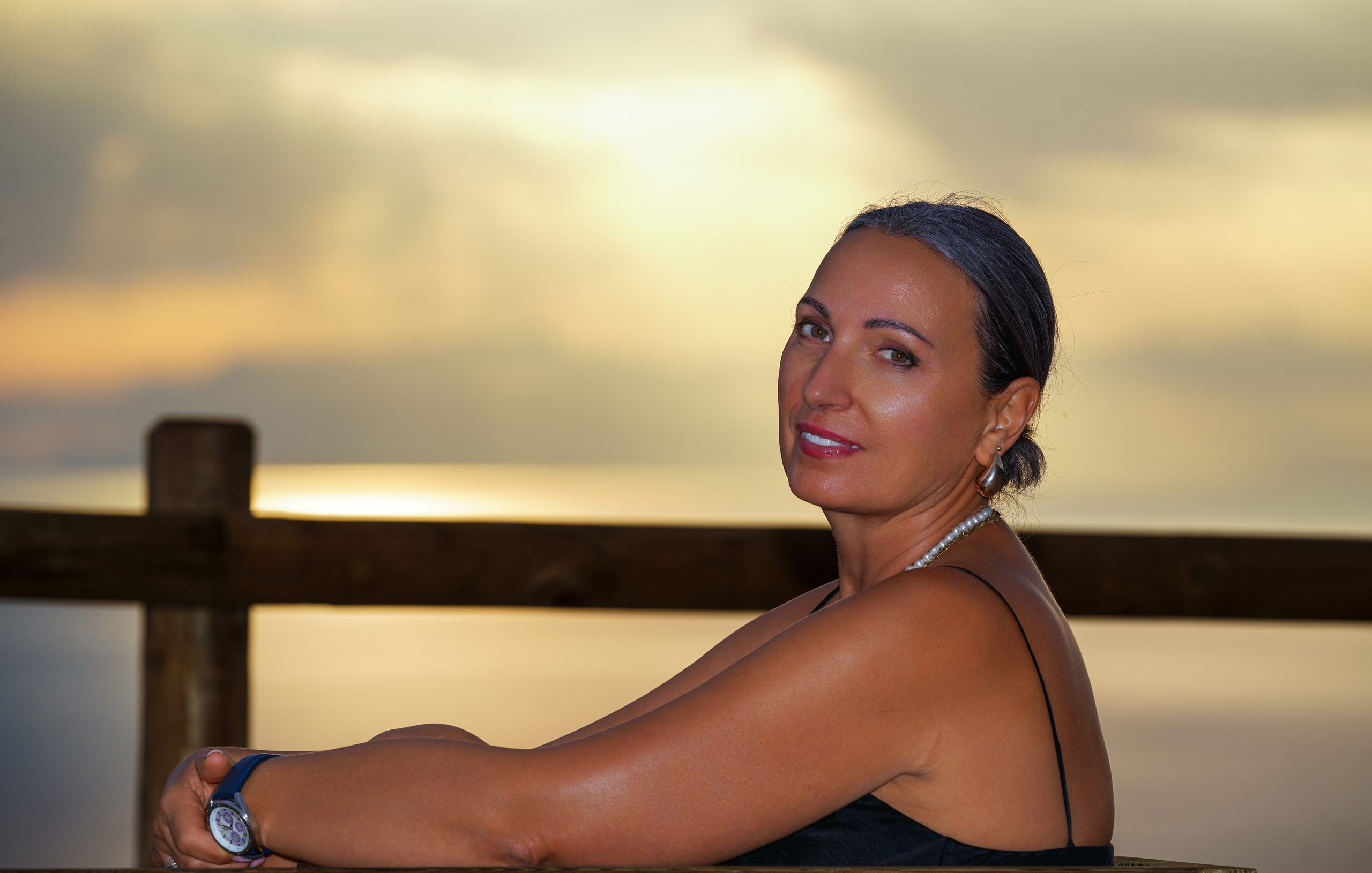 Woman looking back over her shoulder beside a wooden fence, golden sunset sky behind — Cerro Gordo, La Herradura