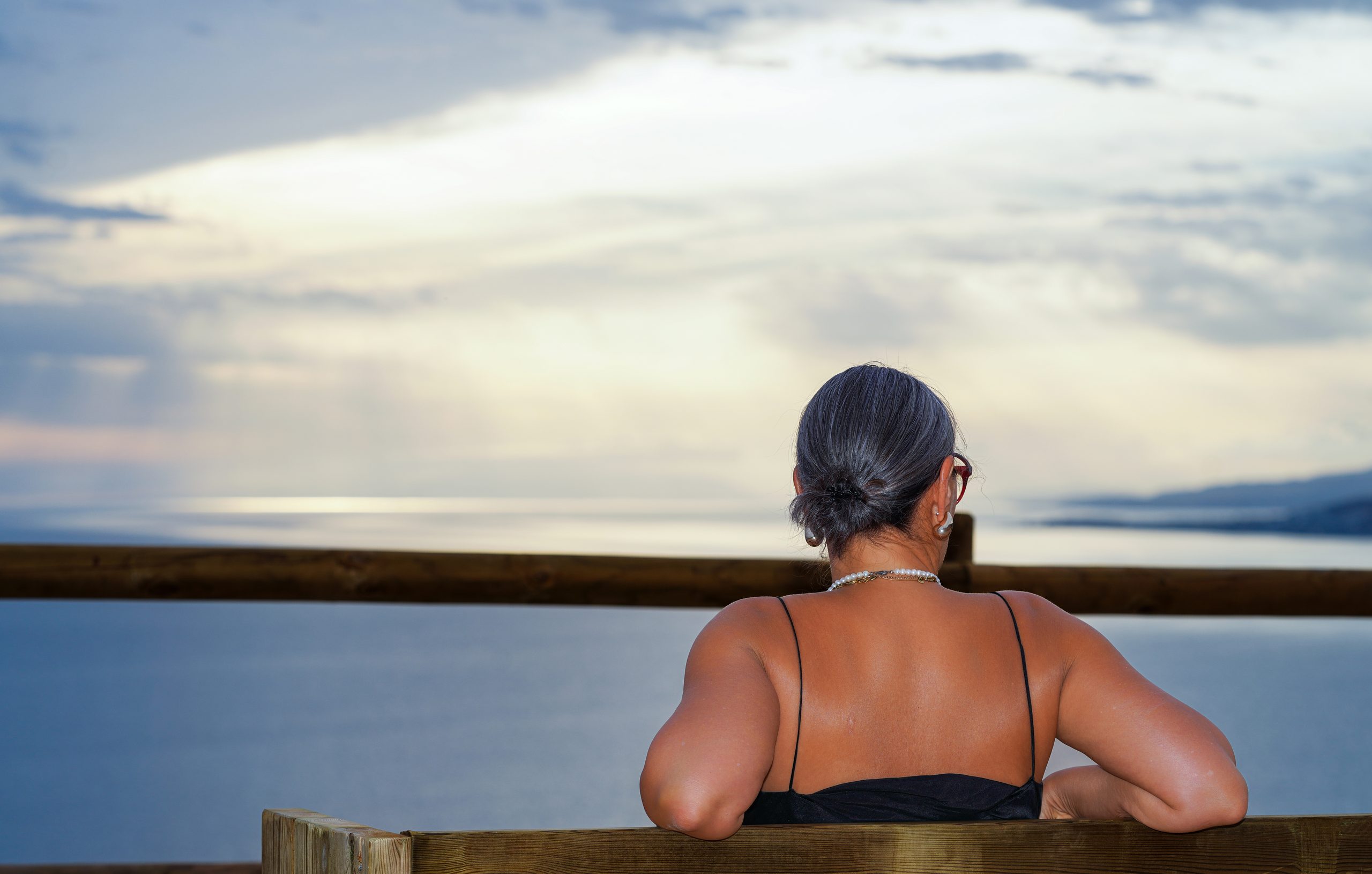 Woman seen from behind on a wooden bench, looking out over the sea at dusk — Cerro Gordo, La Herradura