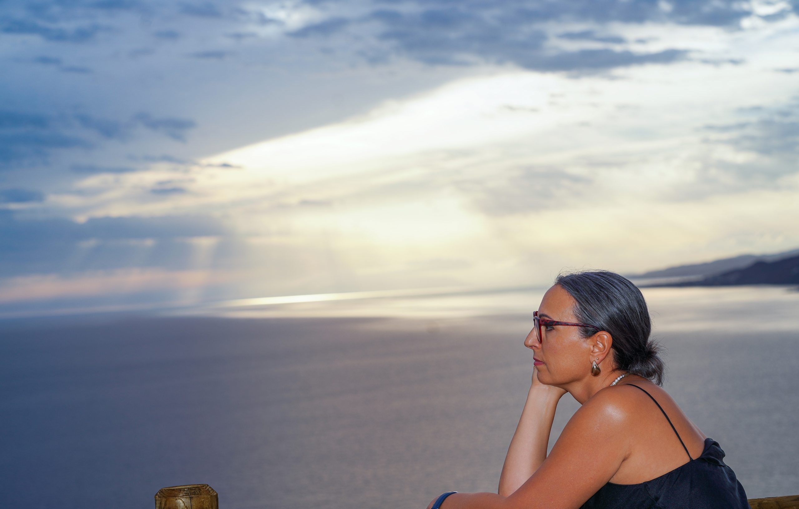 Woman in profile, chin resting on her hand, gazing over the sea from a clifftop bench — Cerro Gordo, La Herradura