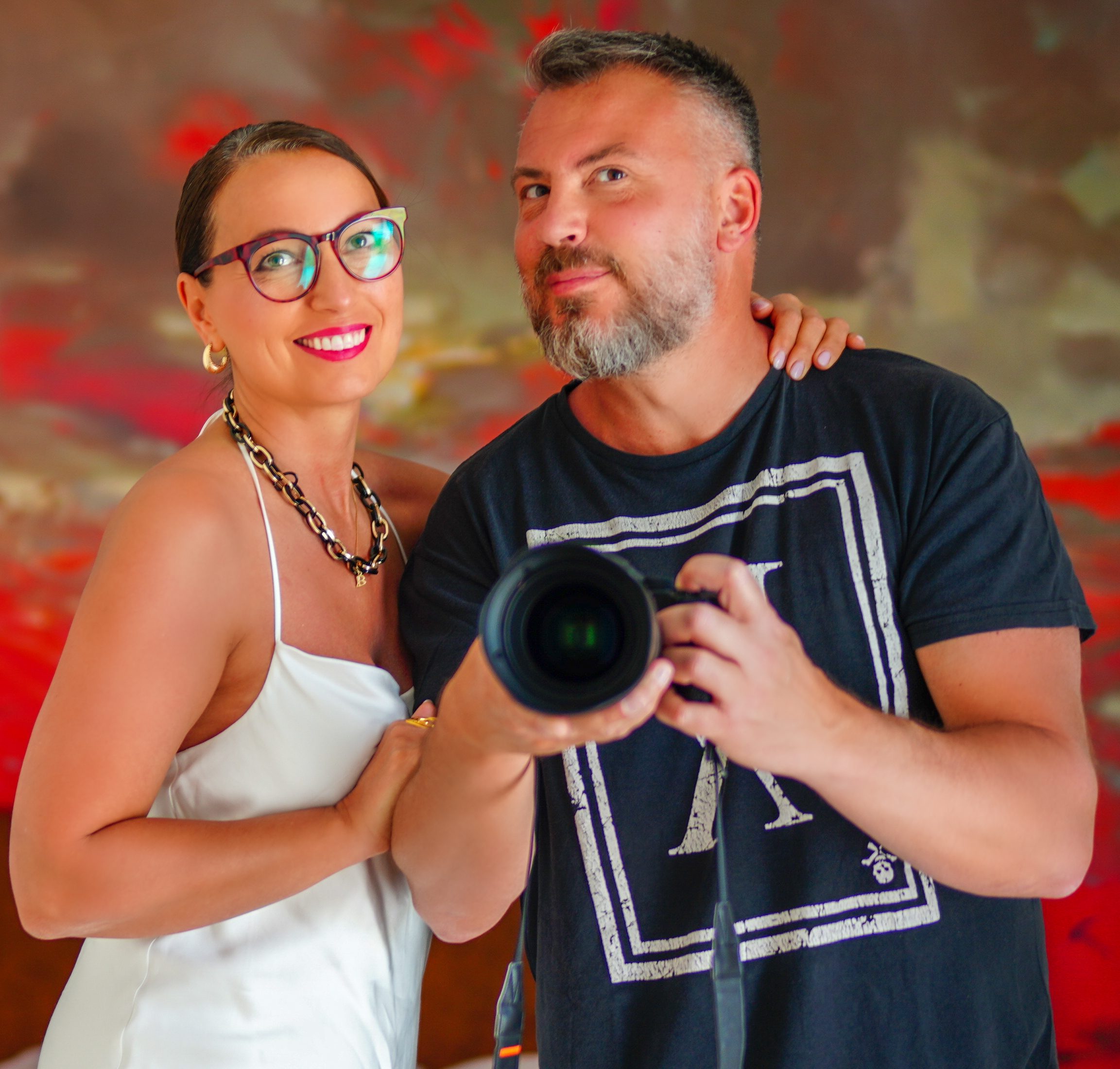 Couple souriant devant un tableau rouge, l'homme tenant un appareil photo