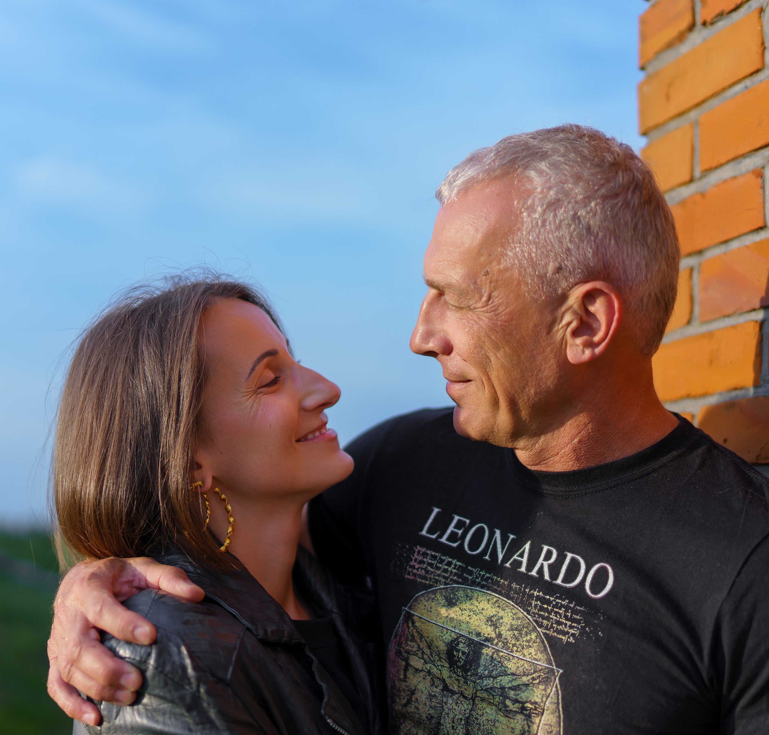Couple qui se sourit devant un ciel bleu et un mur de briques