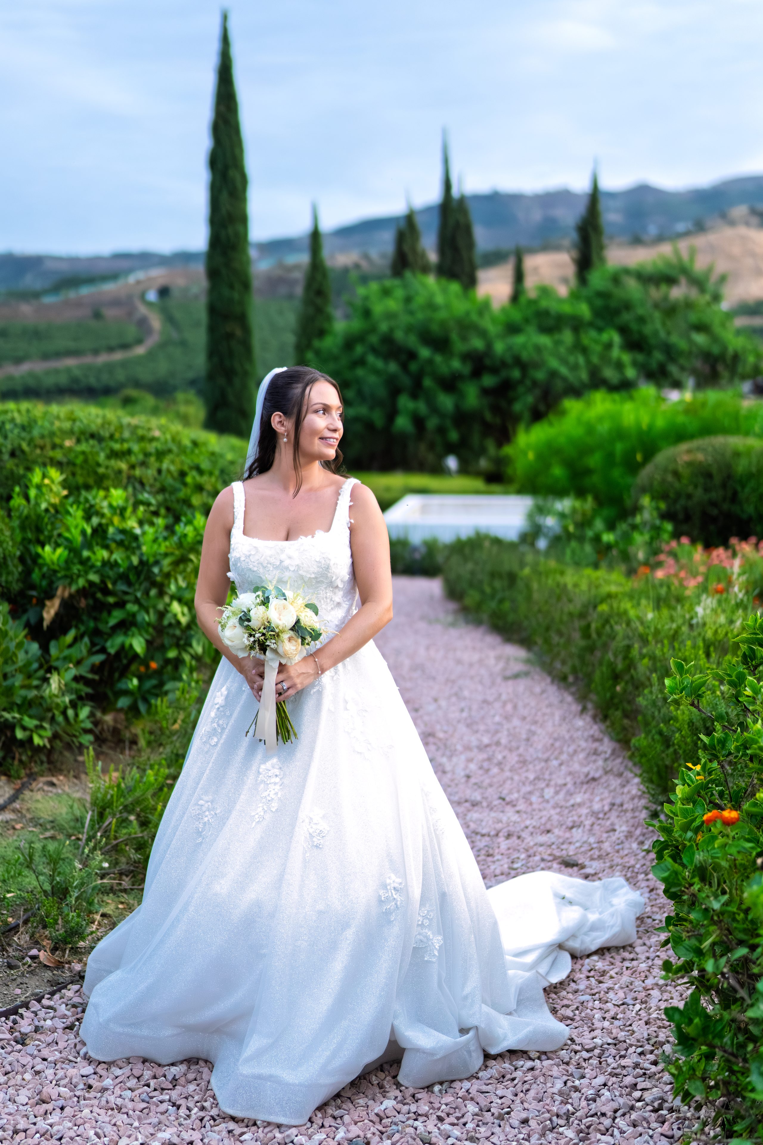 La novia con su ramo en un camino de grava rosa entre setos — Cortijo Bravo, Vélez-Málaga