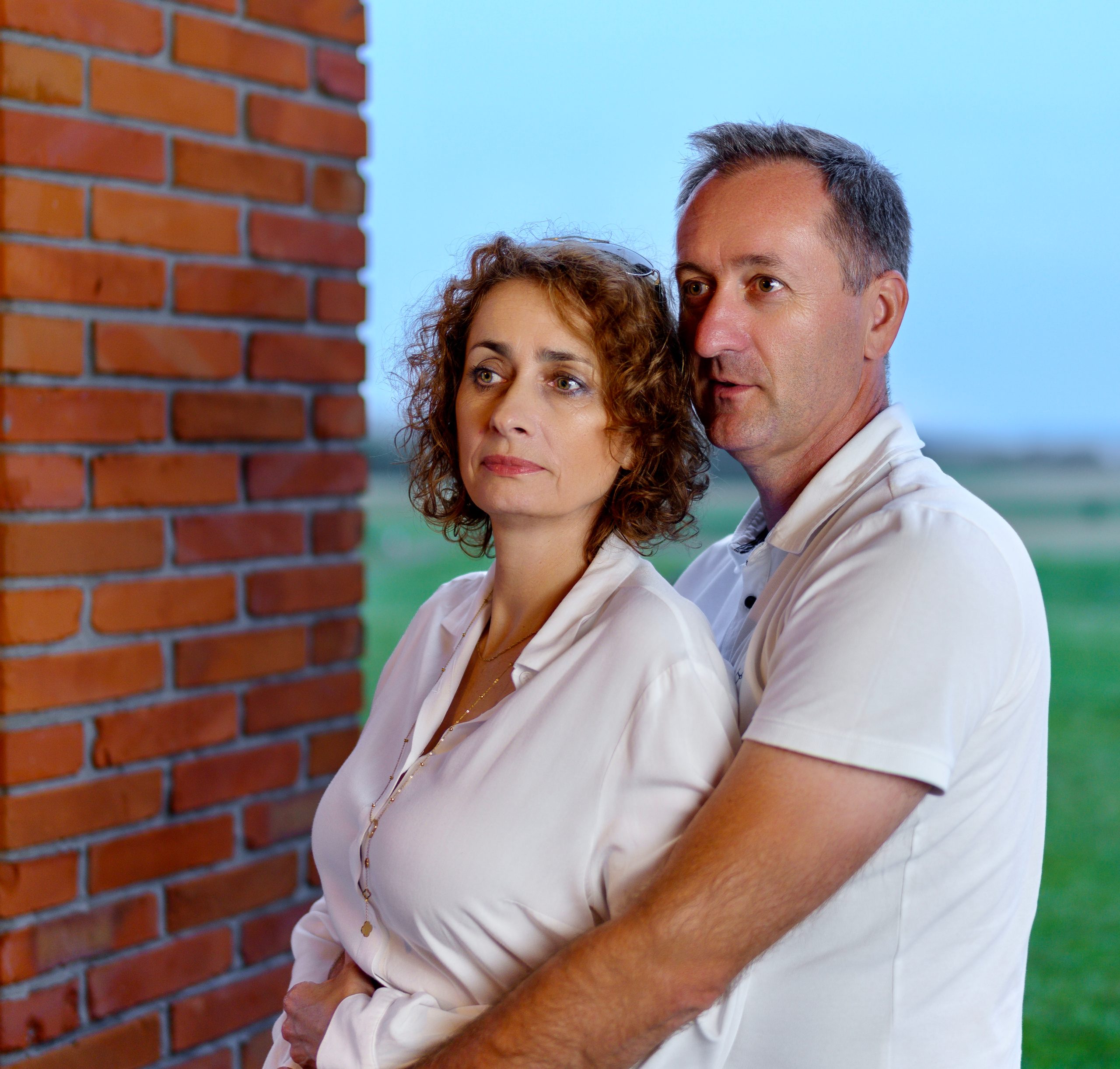 Couple enlacé près d'un pilier en briques, regardant l'objectif