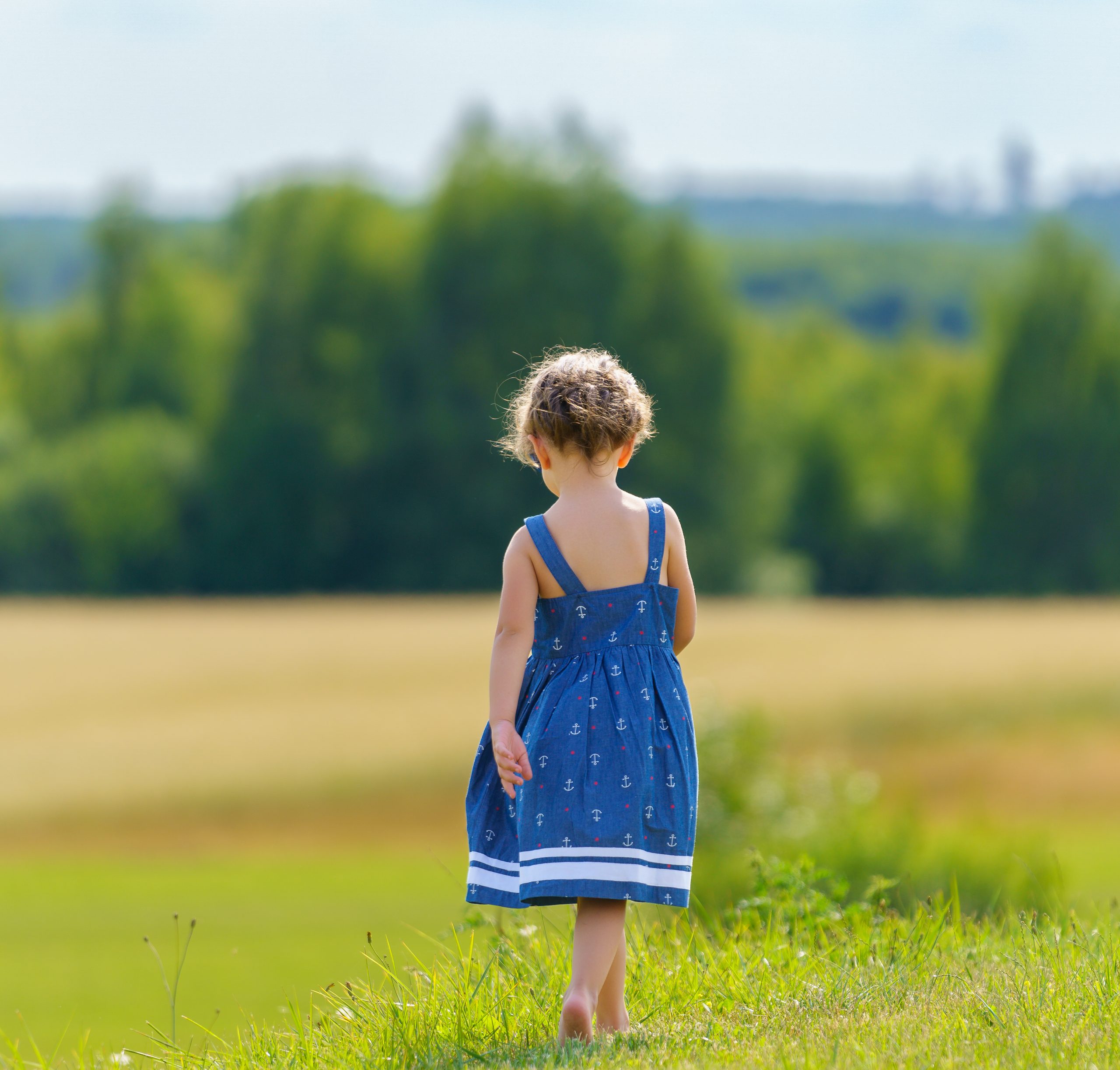 Niña con vestido azul caminando hacia un trigal