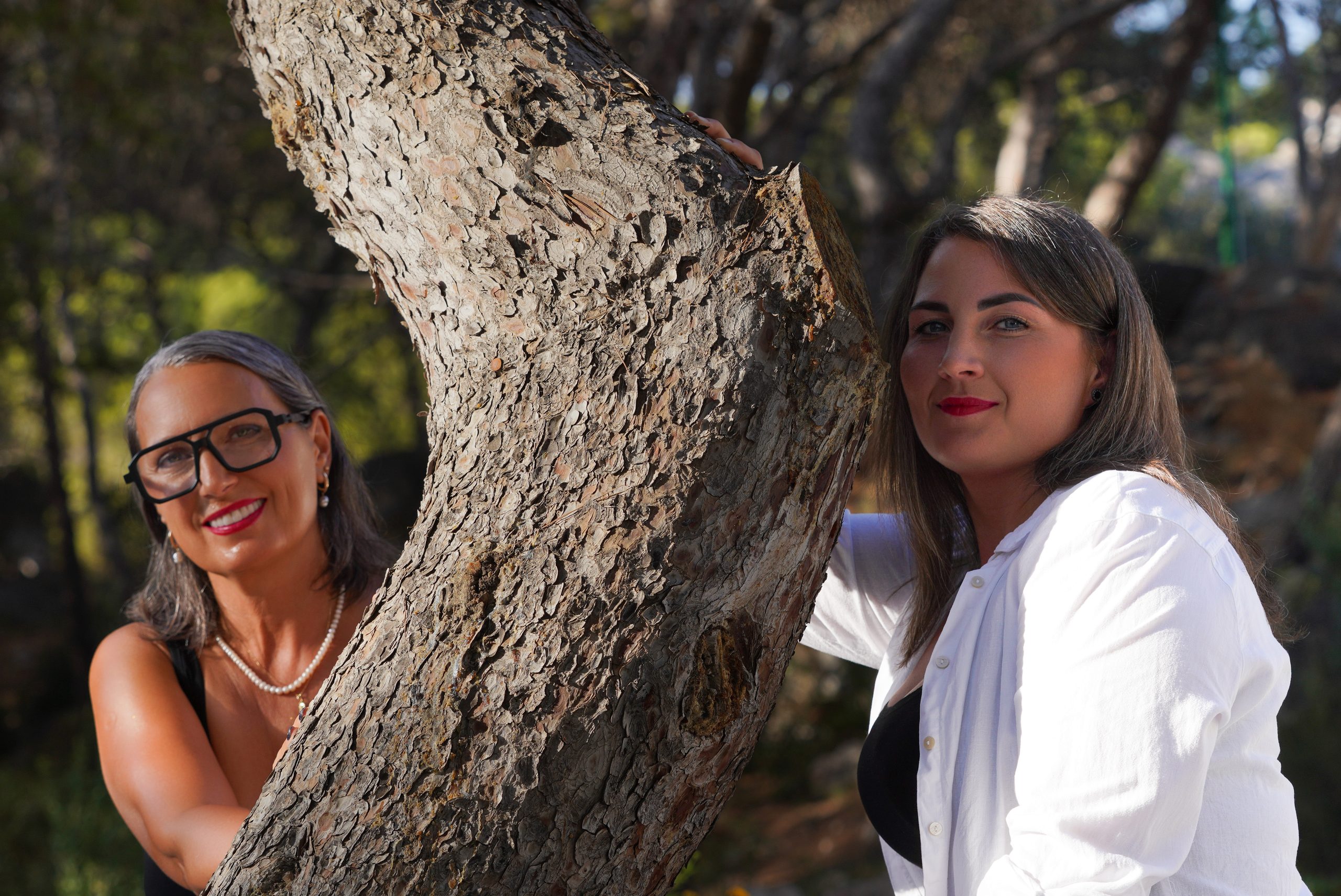 Dwie kobiety po obu stronach pochylonego pnia sosny — Ermita, Marina del Este