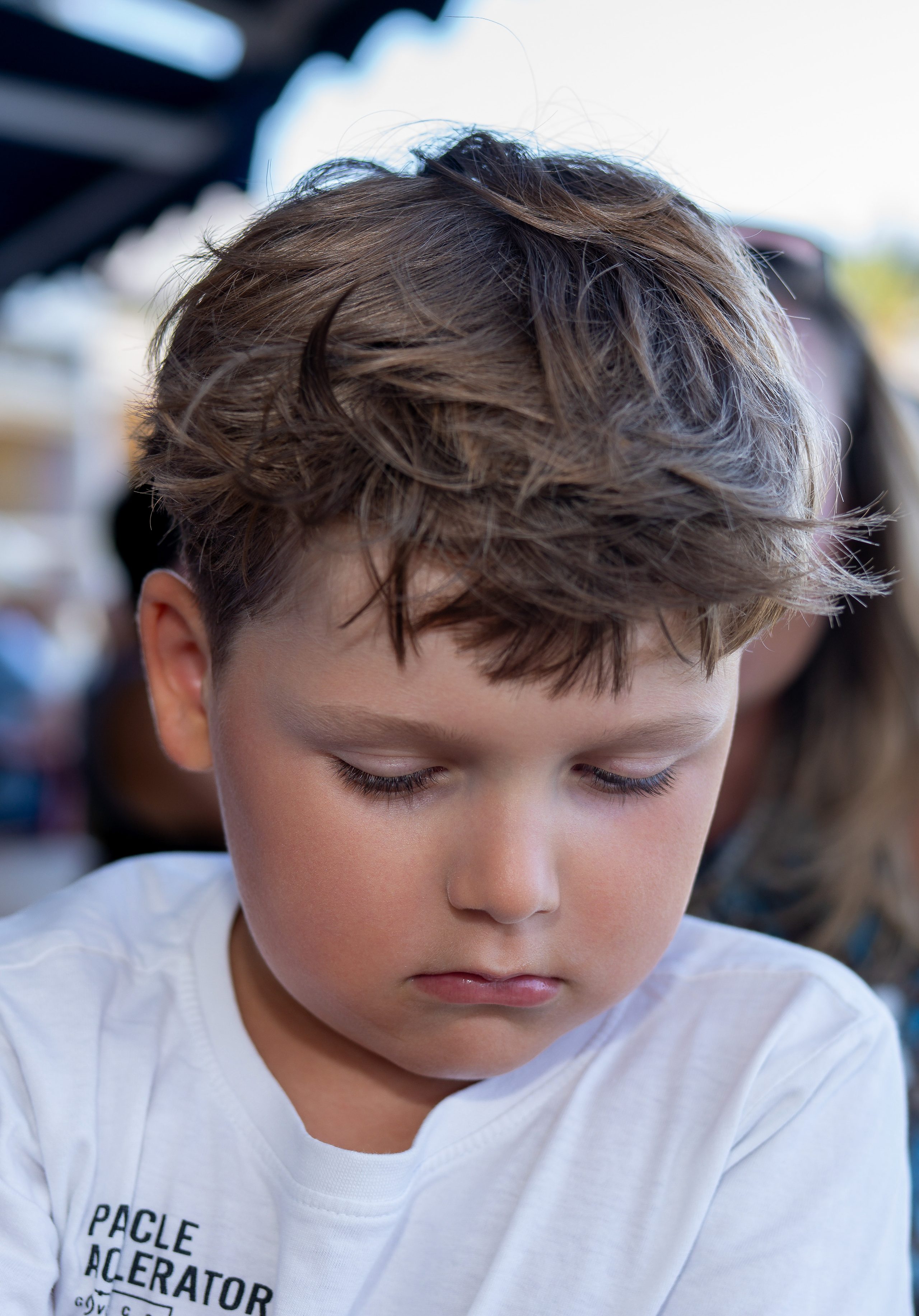 Close-up of a boy with tousled hair in a white T-shirt, looking down